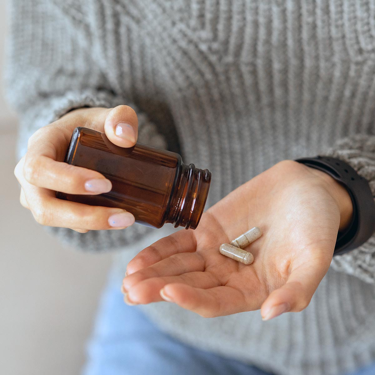 Woman pouring nutritional supplement capsules into her hand from a glass bottle