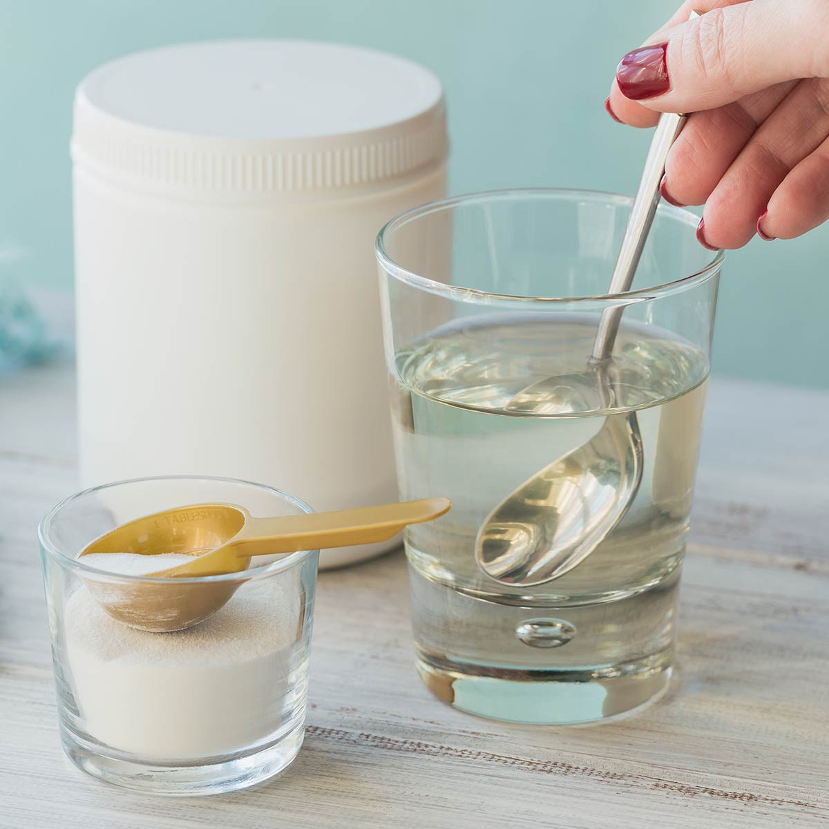 collagen powder in a tub and a scoop and a glass of water