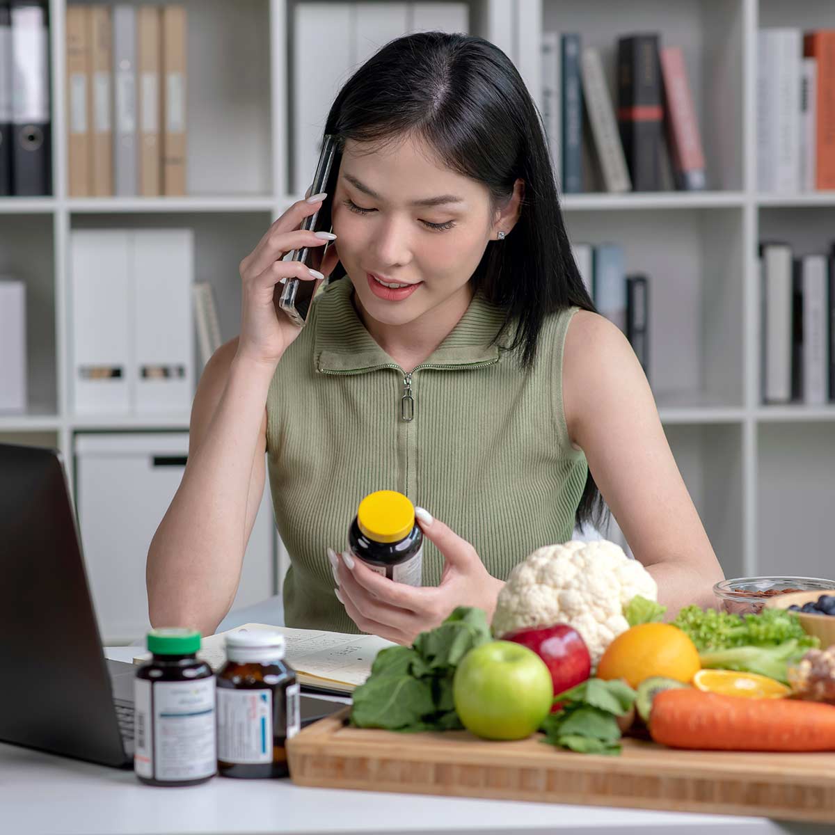 woman looking at nutritional capsule bottle in front of a laptop