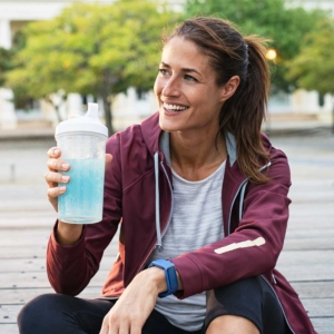 a woman drinking an electrolyte beverage on a break from jogging