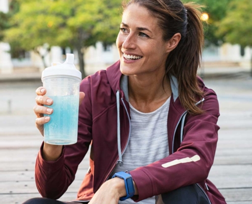 a woman drinking an electrolyte beverage on a break from jogging
